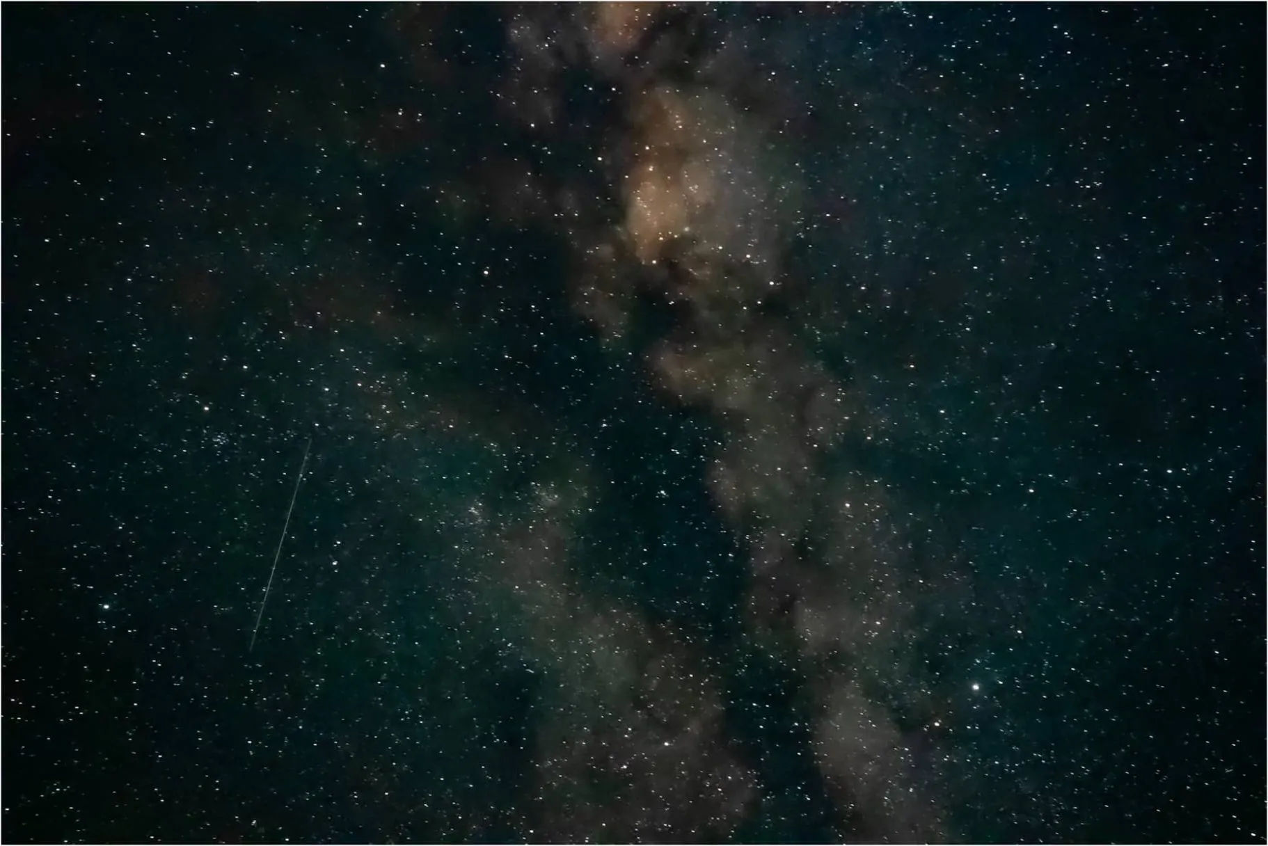 The Milky Way across a dark sky, with the streak of a satellite at the lower left