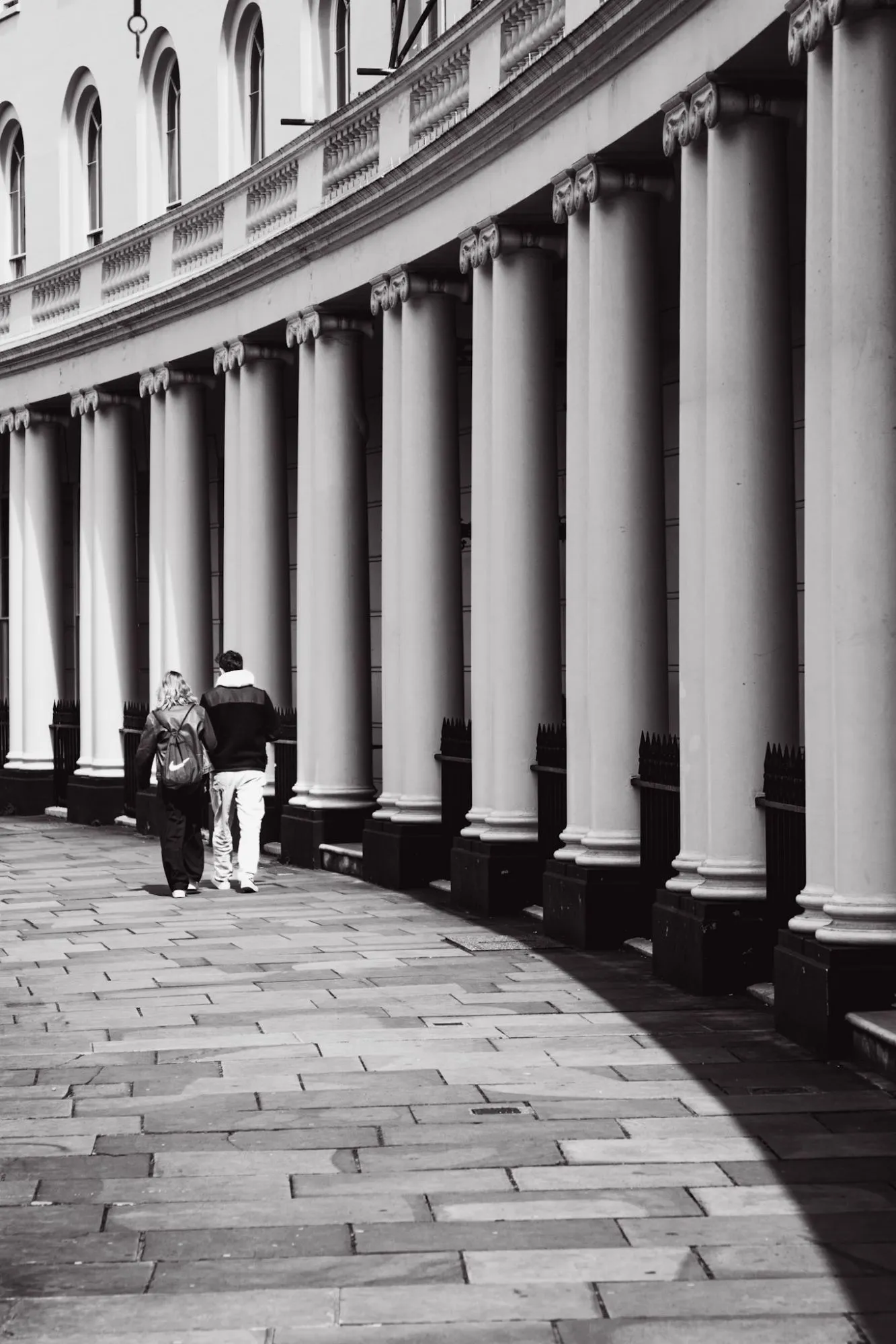Black and white: a couple walks along a curved colonnade, half of it in shadow