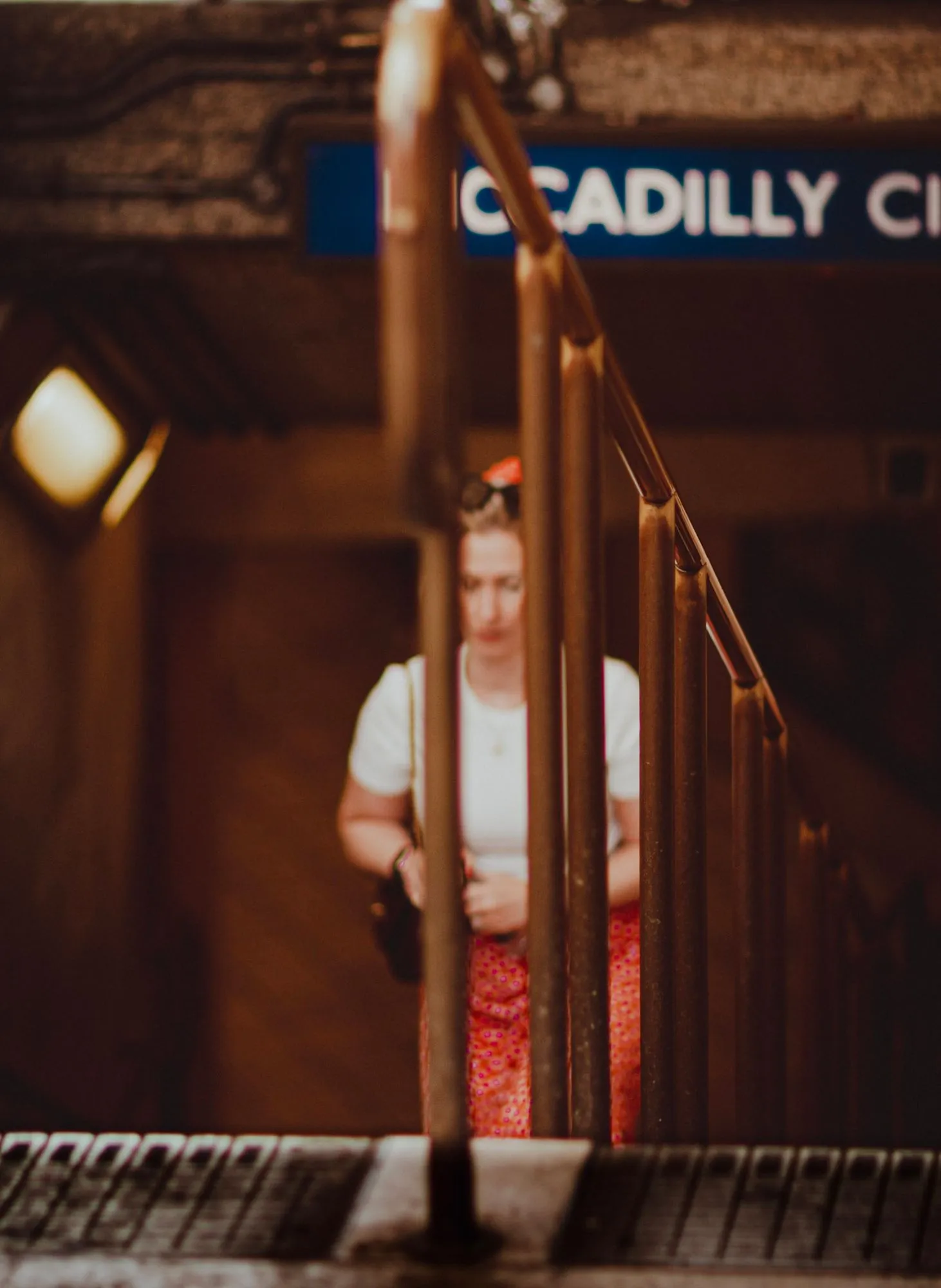 A woman coming up the steps of Piccadilly Circus station, seen through the brass handrails