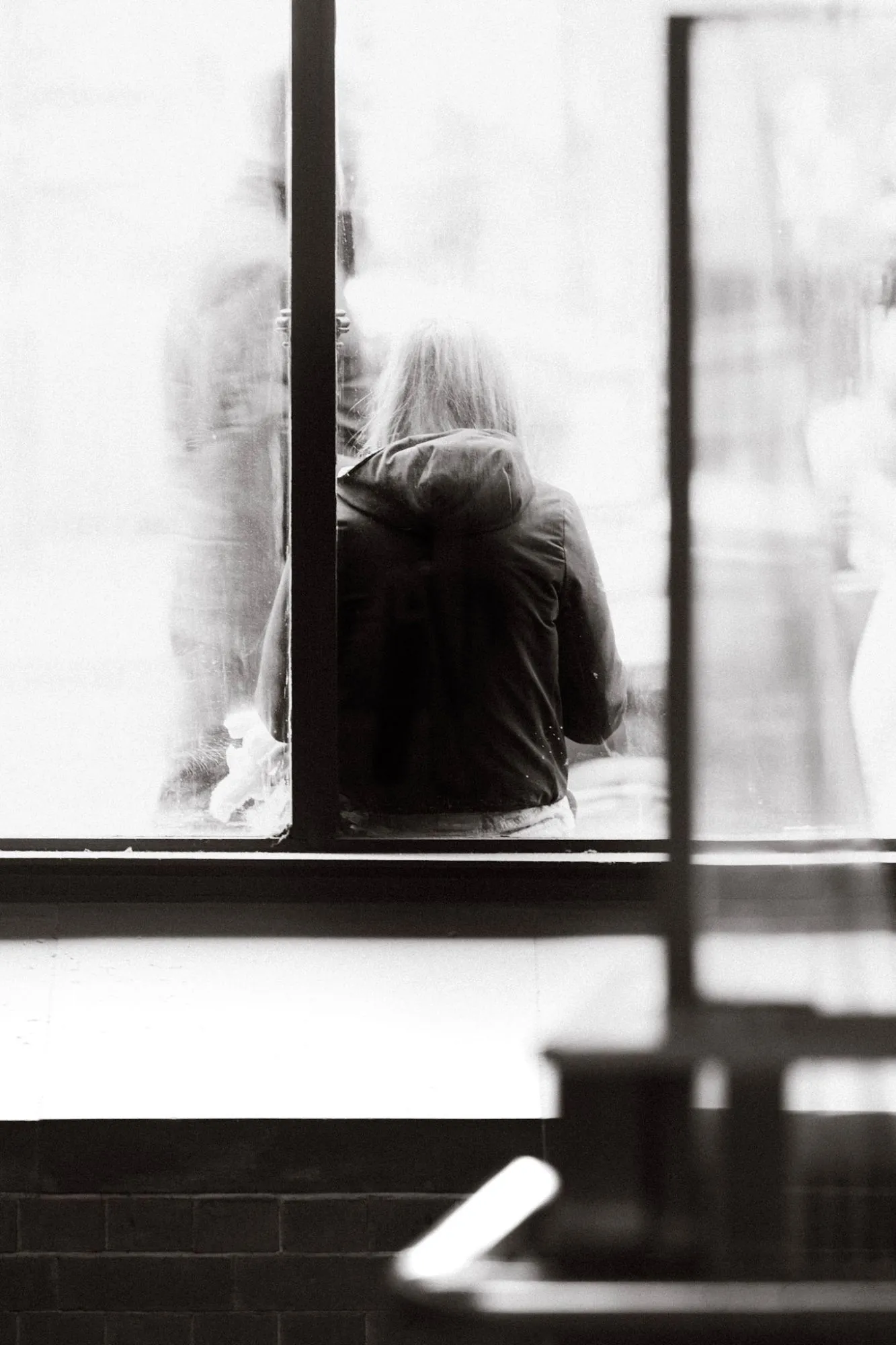 Black and white: a person with long hair, seen from behind through a frosted window