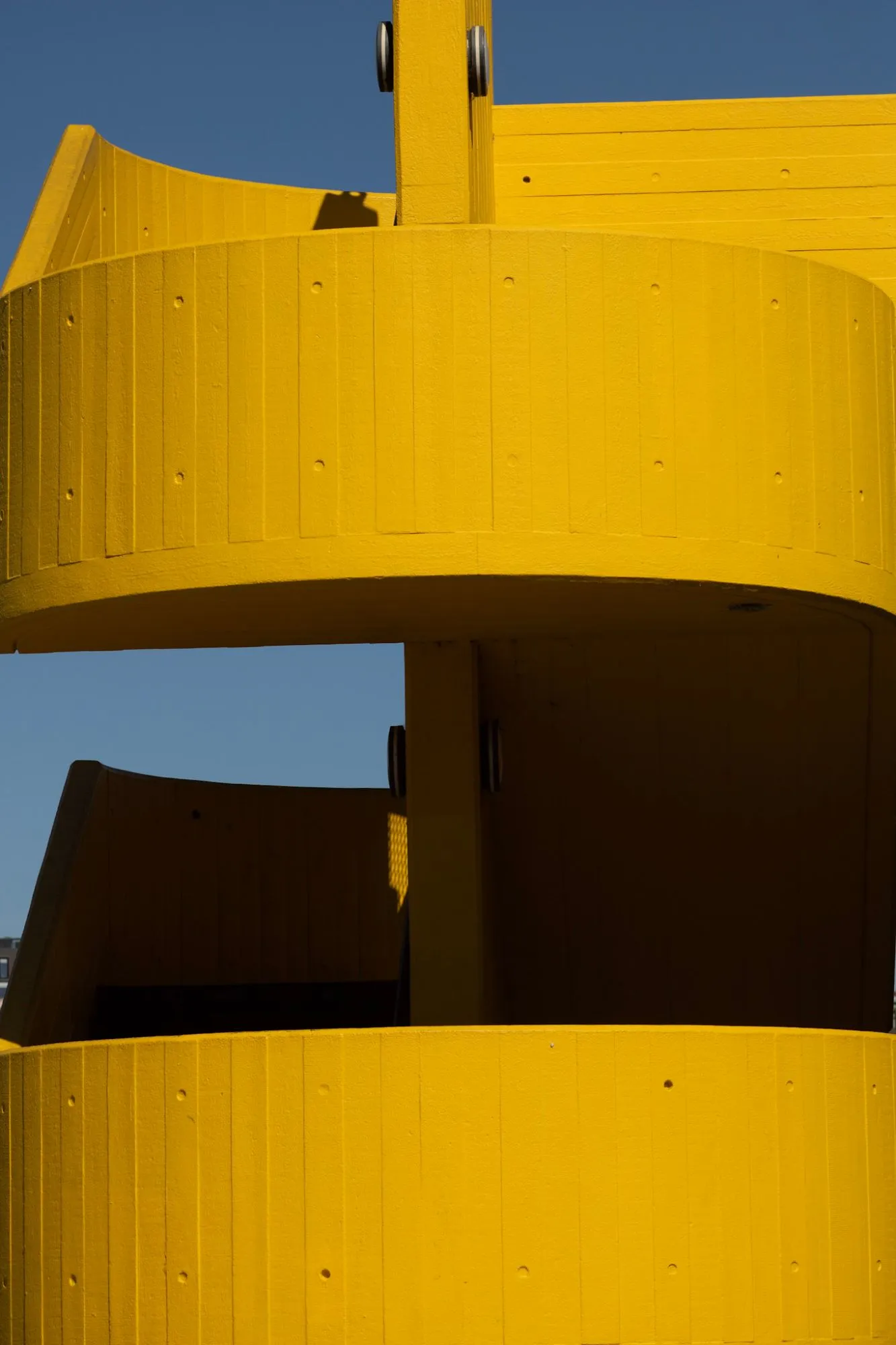 A bright yellow timber structure of curved walls against a deep blue sky